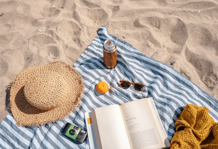 Composição de itens de férias organizados sobre uma toalha na areia da praia, representando um momento de lazer e descanso.