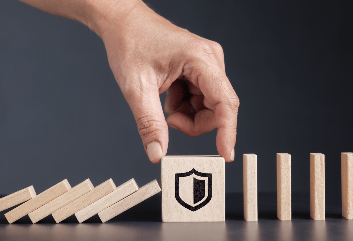 Mão interrompendo efeito dominó com bloco contendo símbolo de escudo, representando proteção jurídica e advocacia preventiva para evitar riscos e problemas legais.