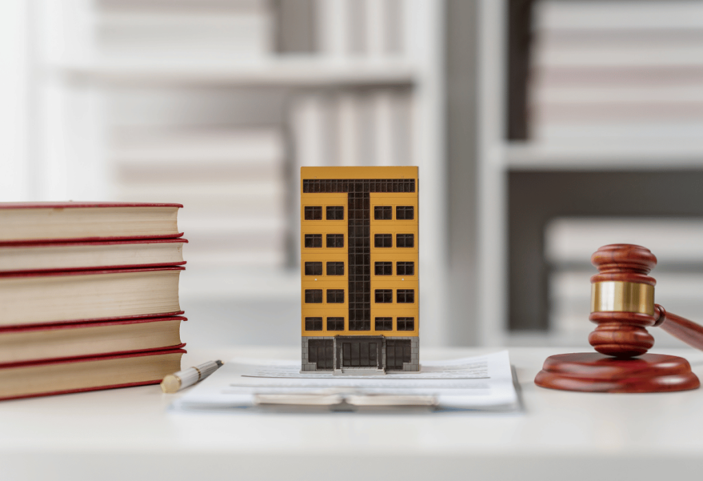 Maquete de prédio com livros jurídicos e martelo de juiz sobre mesa, representando riscos legais na gestão condominial